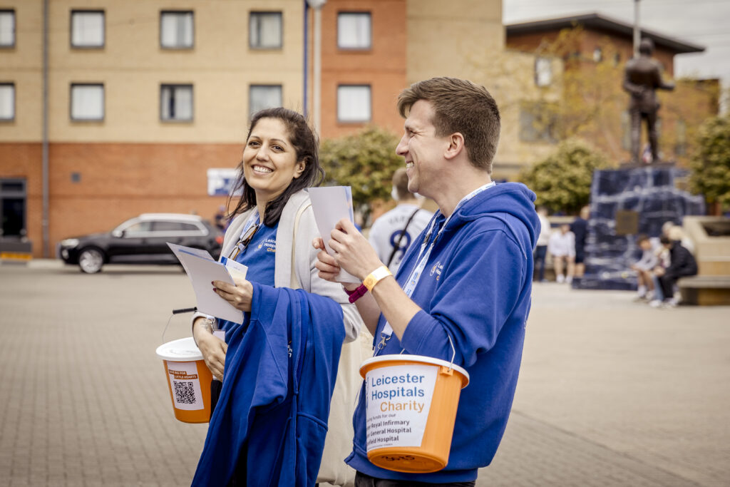 Two Leicester Hospitals Charity colleagues walking with fundraising buckets in uniform
